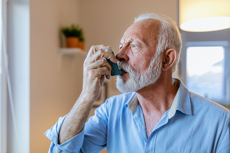 A senior man takes a puff of his inhaler as he manages his comorbidities, a key aspect of supporting a loved one with COPD.