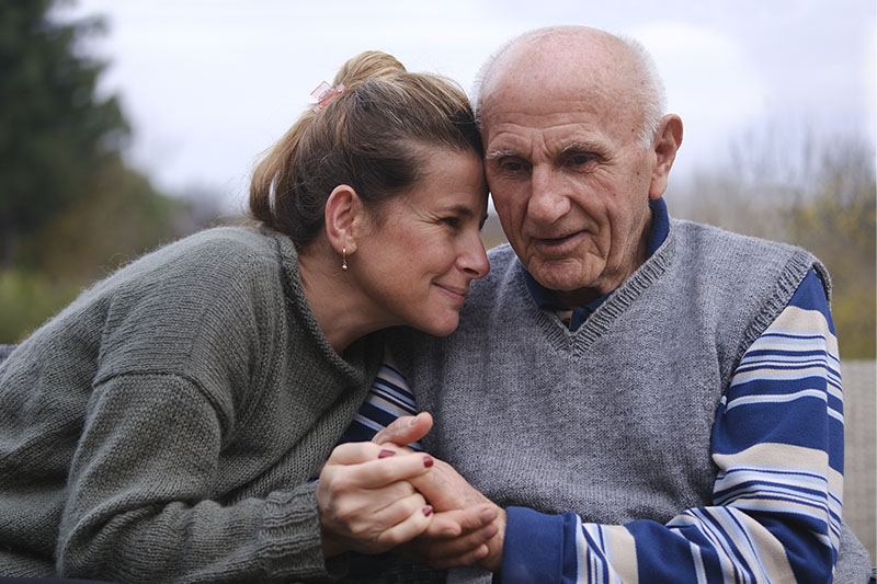 A woman sits with her father, helping him with some of the non-movement symptoms in Parkinson’s.