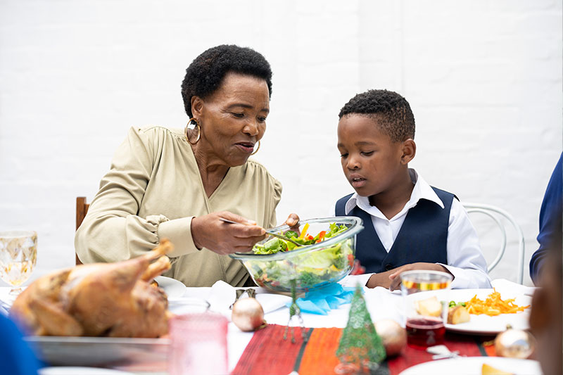 A senior woman takes a serving of salad as she practices healthy eating, managing senior hypertension during the holidays.