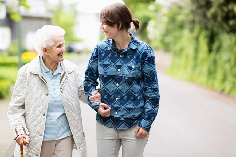 A woman helps her elderly mother take a walk around the block to help her avoid common fall risks for older adults.