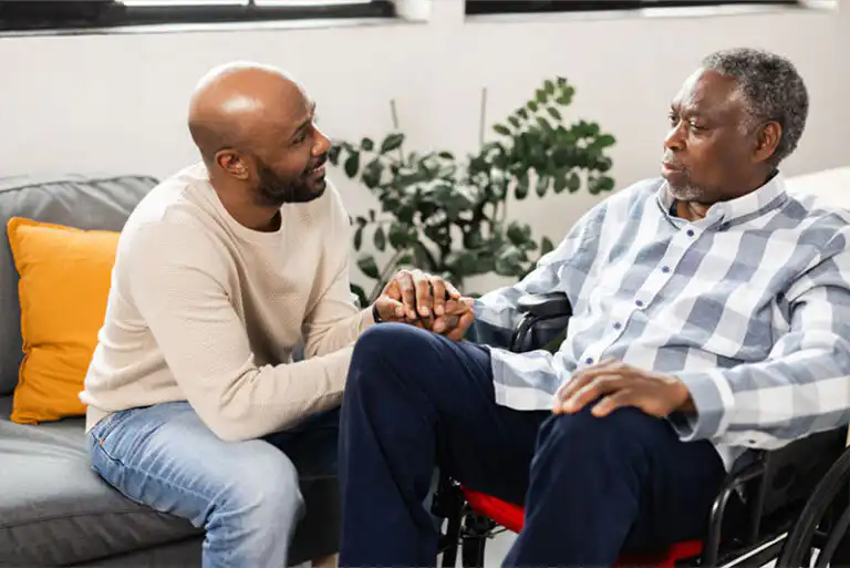 A man holds his elderly father’s hand as they discuss his dementia behavior triggers.