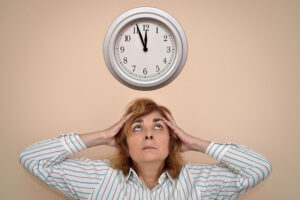 A woman experiencing caregiving burnout looks at the clock as though she doesn’t have enough time to get everything done.