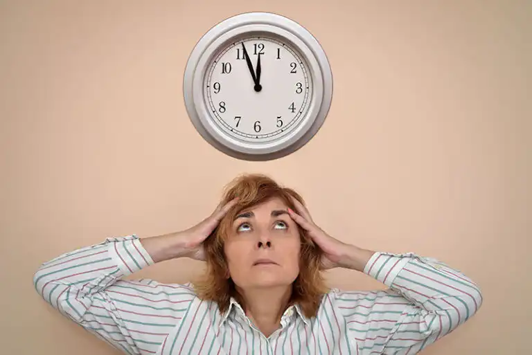 A woman experiencing caregiving burnout looks at the clock as though she doesn’t have enough time to get everything done.